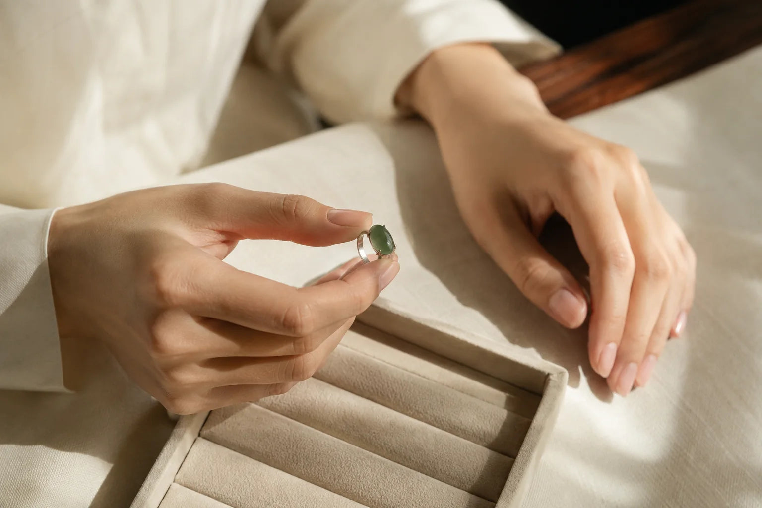 Hands holding an illustrative jade-green ring above a pale suede viewing tray.